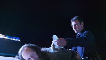 Close-up of a police officer making an arrest, bending the suspect over the hood of his police car and holding a bag of evidence