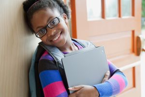 African American elementary student holding books at doorway.