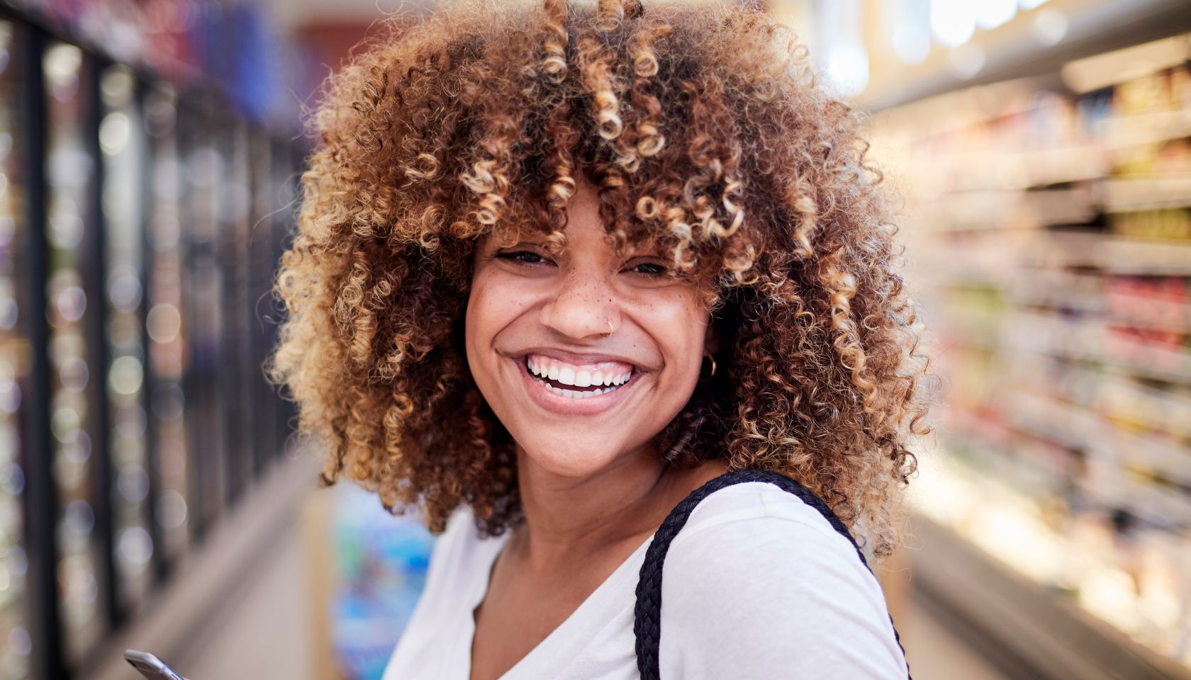 Black woman holding cell phone smiling in grocery store