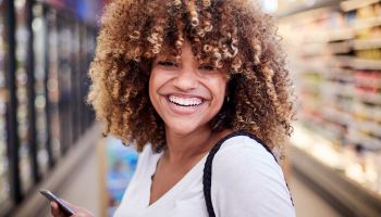 Black woman holding cell phone smiling in grocery store