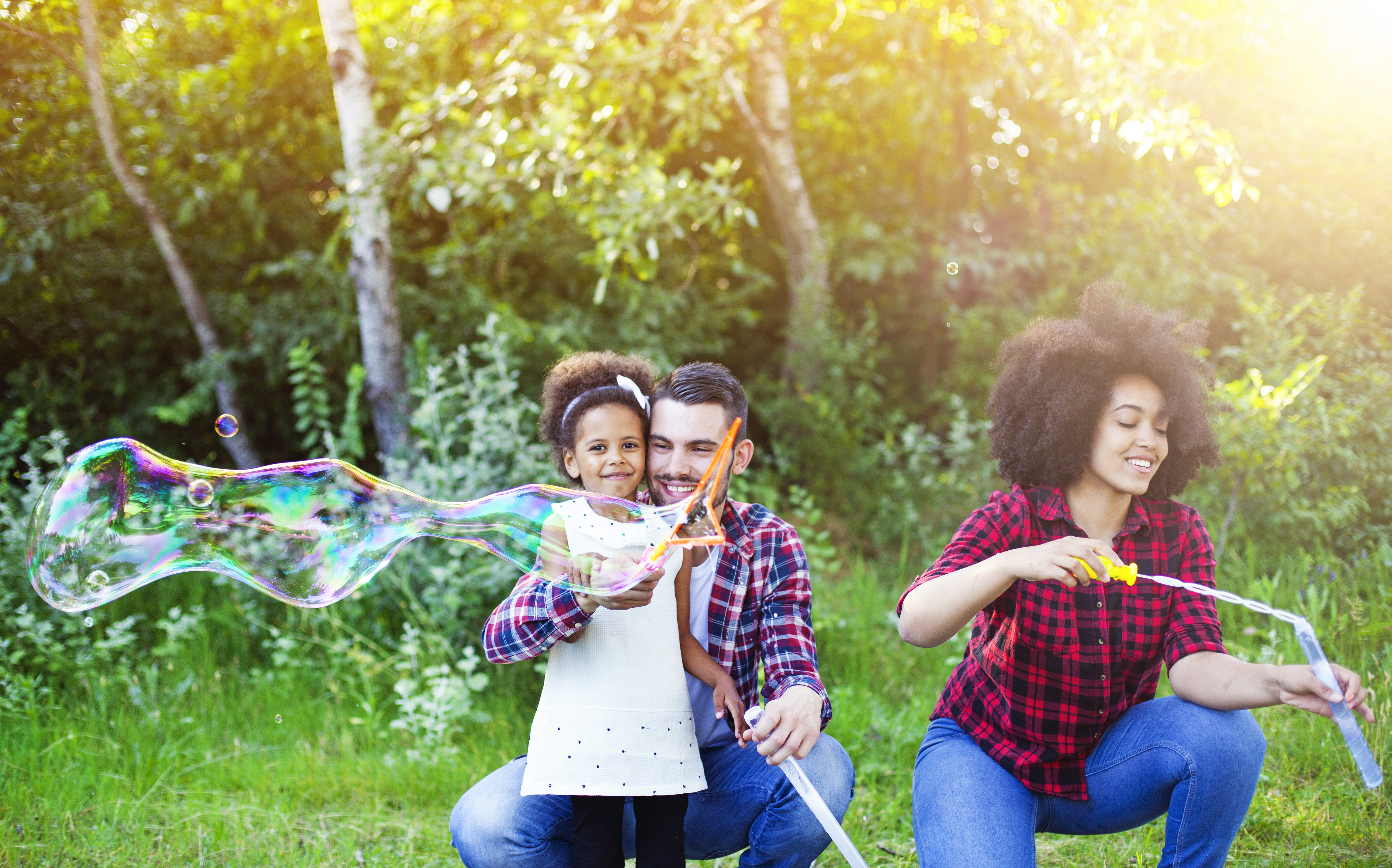 Happy family playing soap bubbles in park.