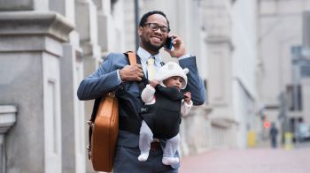 Black businessman with son in baby carrier talking on cell phone