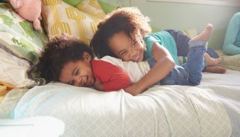 Smiling Black girl tickling baby brother on bed
