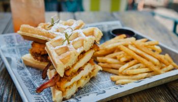 Fried Chicken and bacon waffle sandwich with french fries in an outdoor restaurant setting.