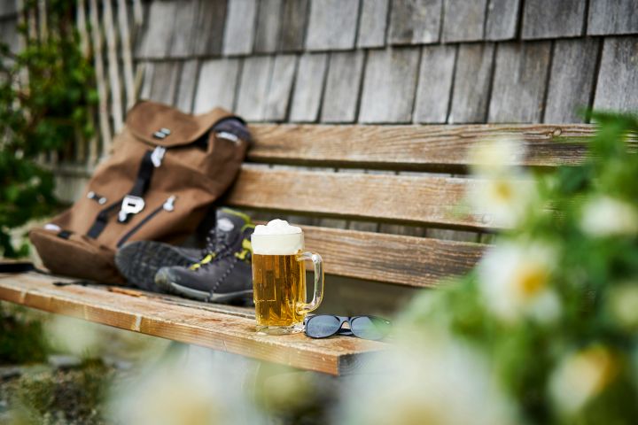 Germany, Bavaria, glass of beer, backpack, sunglasses and hiking shoes on wooden bench