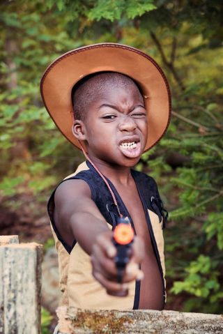 Little black boy playing cowboy with a toy gun.