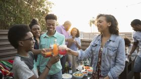 African American family toasting soda glasses, enjoying barbecue on summer deck