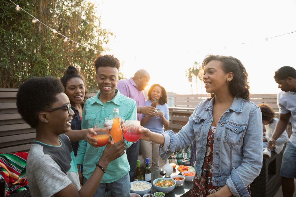 African American family toasting soda glasses, enjoying barbecue on summer deck