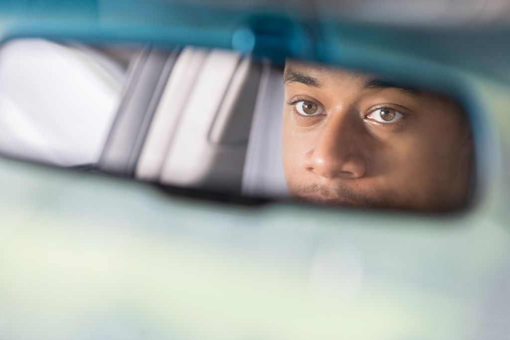 Partial reflection of man looking in rear view mirror