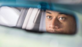 Partial reflection of man looking in rear view mirror