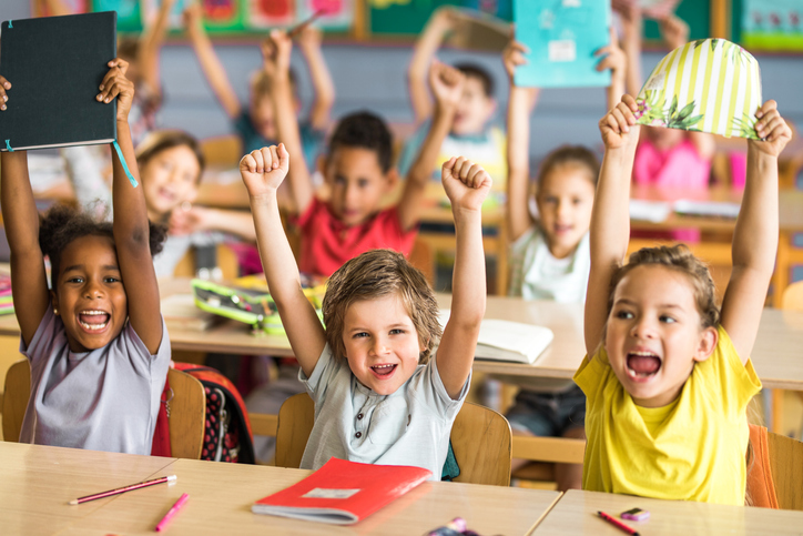 Group of joyful elementary students screaming with raised arms in the classroom.