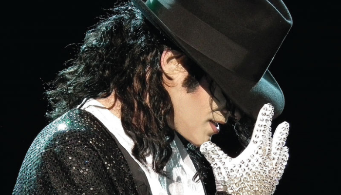 A person wearing a black hat and gloves performing on stage.