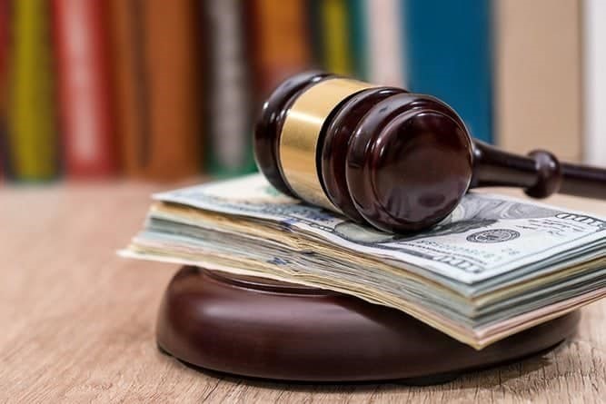 A gavel resting on a stack of US dollar bills on a wooden table, representing the legal system and financial matters.