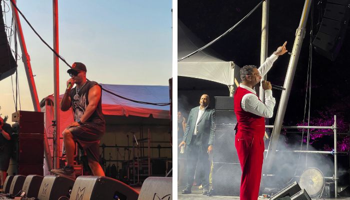 Two men on a stage, one wearing a red jumpsuit and the other a baseball cap, performing in front of a large tent.